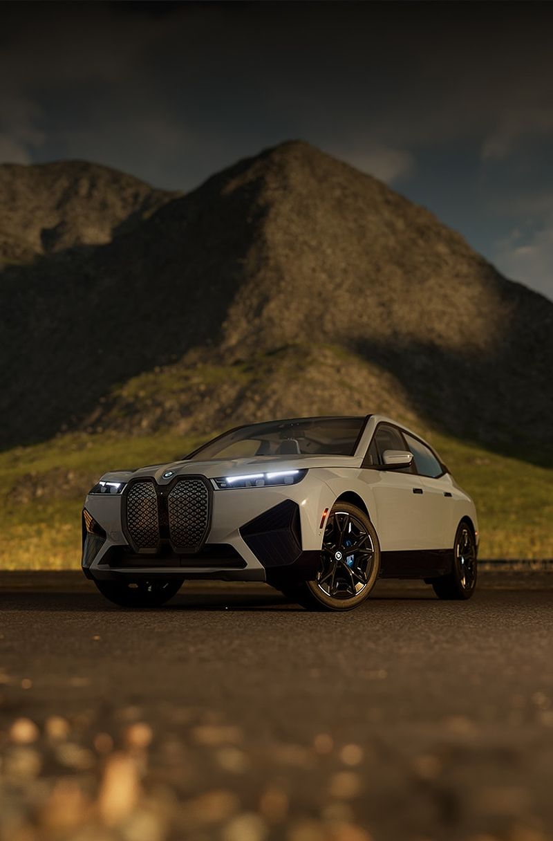 Front three-quarters image of a 2025 BMW iX with headlights on, set in front of a mountain.